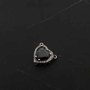Op de afbeelding: Een zilveren hartvormige hanger met een zwarte edelsteen omringd door heldere strass.
