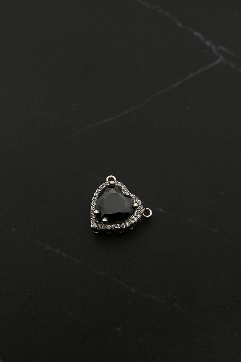Op de afbeelding: Een zilveren hartvormige hanger met een zwarte edelsteen omringd door heldere strass.