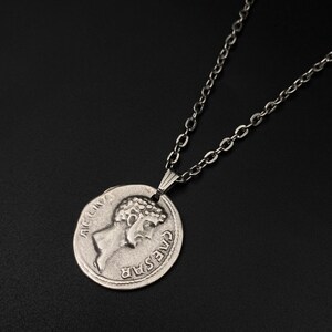 May include: A silver chain necklace with a silver coin pendant featuring a profile of Julius Caesar with the inscription "CAESAR" and "AET.CN.V" on the coin.