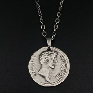 May include: A silver chain necklace with a silver coin pendant featuring a profile of Julius Caesar with the inscription "CAESAR" on the coin.