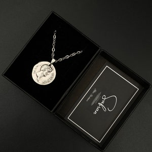 May include: A silver necklace with a round pendant featuring a profile of a woman's face. The necklace is in a black box with a white card that says "Say It With Jewelry".