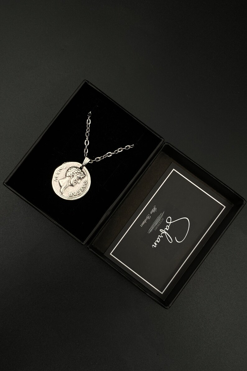 May include: A silver necklace with a round pendant featuring a profile of a woman's face. The necklace is in a black box with a white card that says "Say It With Jewelry".