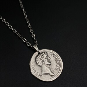 May include: Silver chain necklace with a silver coin pendant featuring a profile of Julius Caesar and the inscription "CAESAR".