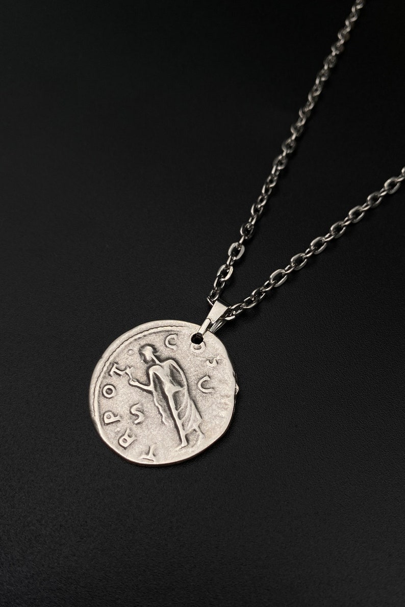 May include: Silver necklace with a round pendant featuring a Roman coin design. The pendant has an inscription that reads "SPQR" and depicts a figure standing with a staff.