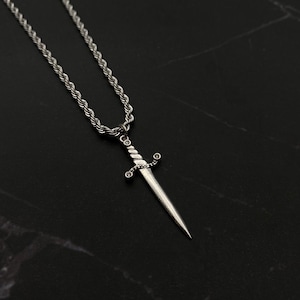 Op de afbeelding: Een zilveren touwketting met een zilveren zwaardhanger. Het zwaard heeft een gedraaid ontwerp en kleine heldere stenen op het handvat.