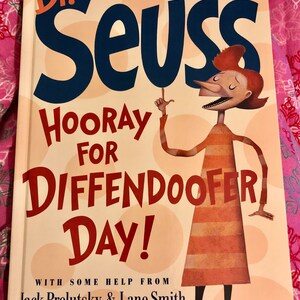 May include: A book cover with a red, white, and blue illustration of a character with a long nose and a striped shirt. The title of the book is "Dr. Seuss Hooray for Diffendoofer Day!" with the text "With some help from Jack Prelutsky & Lane Smith" at the bottom.