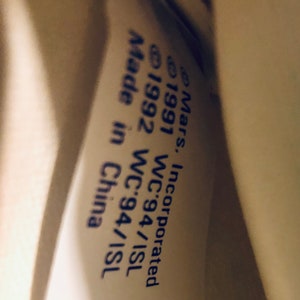 Puede incluir: Primer plano de una etiqueta blanca con texto azul. El texto dice "Mars, Incorporated &copy;1991 WC'94/ISL &copy;1992 WC'94/ISL Made in China."