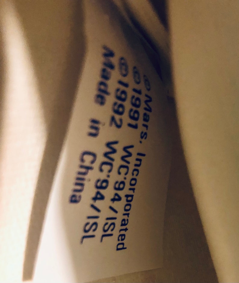 Puede incluir: Primer plano de una etiqueta blanca con texto azul. El texto dice "Mars, Incorporated &copy;1991 WC'94/ISL &copy;1992 WC'94/ISL Made in China."
