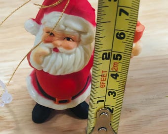 Papá Noel de plástico sosteniendo un adorno de campana para el árbol