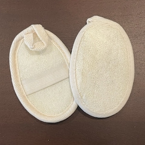 May include: Two white oval-shaped bath sponges with a textured surface. One sponge has an elastic band around the edge.