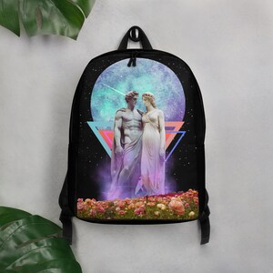 Puede incluir: Mochila negra con un diseño celestial. Presenta estatuas de un hombre y una mujer, un cielo estrellado y una forma geométrica colorida. Las estatuas están en un campo de flores. La mochila tiene un asa superior y correas ajustables.