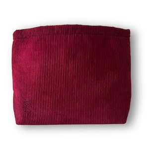 Pode incluir: Uma bolsa de veludo cotel&ecirc; bord&ocirc; com formato retangular. A bolsa tem uma textura canelada e um fecho com cord&atilde;o. O canto inferior esquerdo apresenta um logotipo bordado. O fundo &eacute; branco.