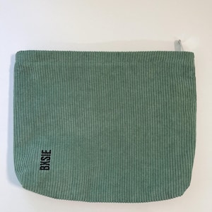 Pode incluir: Uma bolsa de veludo cotel&ecirc; verde s&aacute;lvia com fecho de correr. A bolsa tem uma textura canelada vertical e a palavra "BKSJE" impressa em preto no canto inferior esquerdo. Fundo branco liso.