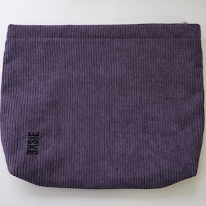 Pode incluir: Uma bolsa retangular de veludo cotel&ecirc; roxo com nervuras verticais. A bolsa tem um fecho de correr na parte superior e a palavra "BKSJE" &eacute; bordada em preto no canto inferior esquerdo. A bolsa est&aacute; sobre um fundo branco.
