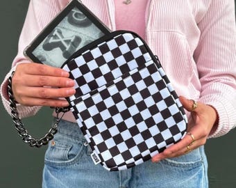 Pode incluir: Uma bolsa transversal xadrez em preto e branco com uma alça de corrente prateada. A bolsa tem um bolso frontal e o texto "BXSIS" no canto inferior direito. Um leitor de e-books é visível dentro da bolsa.