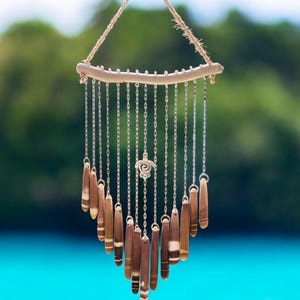 May include: A handcrafted wind chime featuring a driftwood branch, silver chains, and wooden pendants. A decorative silver turtle charm hangs in the center. The pendants are brown with white and tan accents. The chime is suspended by a natural fiber rope.