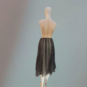Puede incluir: Falda de encaje negro exhibida en un maniqu&iacute;. La falda presenta paneles verticales con intrincados detalles de encaje, con un dise&ntilde;o transparente y fluido. El dobladillo de la falda es asim&eacute;trico.