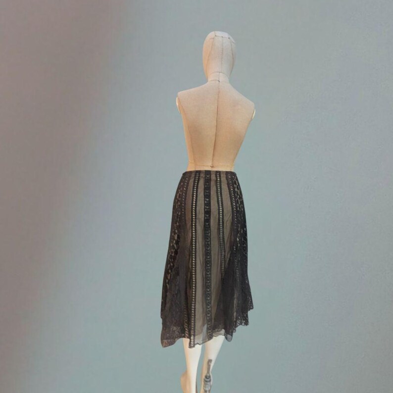Puede incluir: Falda de encaje negro exhibida en un maniqu&iacute;. La falda presenta paneles verticales con intrincados detalles de encaje, con un dise&ntilde;o transparente y fluido. El dobladillo de la falda es asim&eacute;trico.