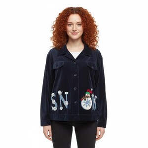 May include: Navy blue corduroy jacket with a button-up front and two chest pockets. The jacket features the word "SNOW" appliqued with snowflakes and a snowman design. The jacket is worn over a white top and black pants.