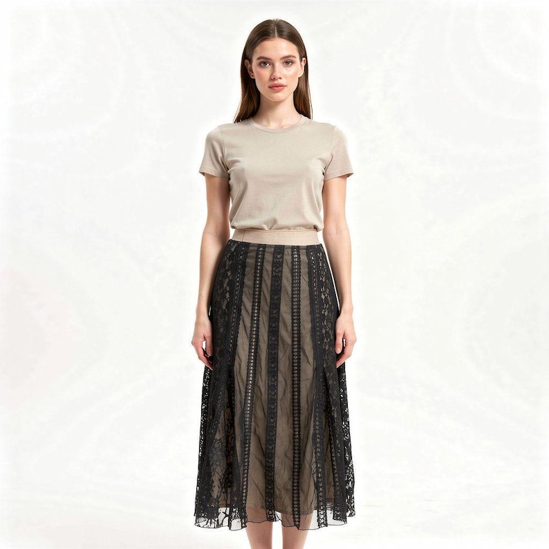 Puede incluir: Una mujer con una camiseta beige de manga corta y una falda midi de encaje negro. La falda tiene paneles verticales de encaje sobre un forro beige. El conjunto se presenta sobre un fondo blanco liso, destacando el dise&ntilde;o y la textura de la ropa.