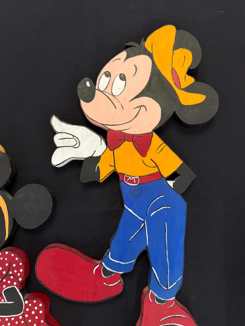 May include: Wooden cutout of Mickey Mouse in a walking pose. Mickey is wearing a yellow shirt, blue pants, red shoes, and a red bow tie. His ears are black, and he has a yellow hat. The cutout is painted with bright colors and has a cartoon style.