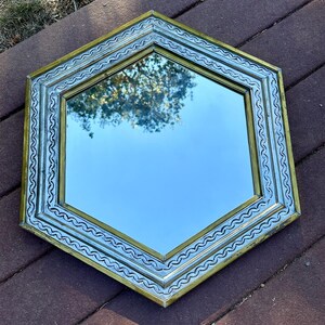 May include: A hexagonal mirror with a silver and gold frame. The frame has a decorative, wavy pattern.