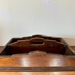 May include: A vintage wooden tray with multiple compartments. The tray has a dark brown finish and a simple design.