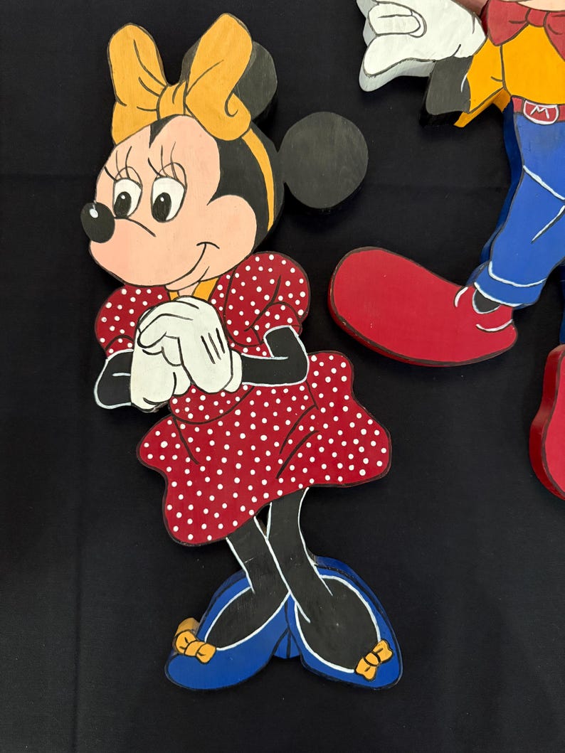 May include: Wooden cutout of Minnie Mouse in a red polka dot dress, yellow bow, and blue shoes. The character is smiling with white gloves and black ears. Part of a larger Disney-themed set.