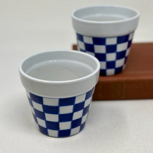 May include: Two white ceramic flower pots with a blue and white checkered pattern.