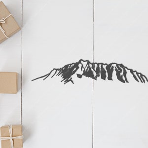 Op de afbeelding: Een zwart silhouet van een bergketen op een witte houten achtergrond. Er zijn verschillende kleine bruine cadeaudoosjes op het oppervlak.