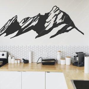 Pu&ograve; includere: Decorazione da parete in metallo nero a forma di catena montuosa in un ambiente da cucina moderno. La decorazione &egrave; montata su una parete bianca sopra un bancone da cucina con armadietti bianchi e una stufa in acciaio inox.