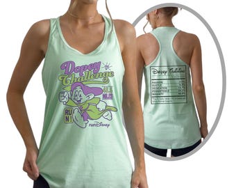 May include: A light green tank top with a graphic of Dopey from Snow White and the Seven Dwarfs, with the text "Dopey Challenge" and "runDisney". The back of the tank top has a nutrition facts label. The model is wearing black shorts.