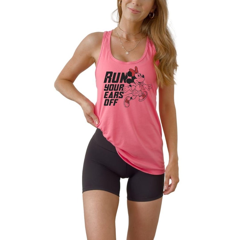 May include: A bright pink racerback tank top featuring a black graphic of a cartoon mouse character in running shoes and the text "RUN YOUR EARS OFF" in bold black lettering, paired with solid black athletic shorts that reach mid-thigh.