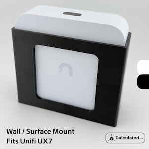 Pode incluir: Um suporte de parede preto com uma abertura quadrada, segurando um dispositivo branco. O dispositivo tem um topo curvo e um logotipo visível no centro. O texto na parte inferior diz "Wall / Surface Mount Fits Unifi UX7".