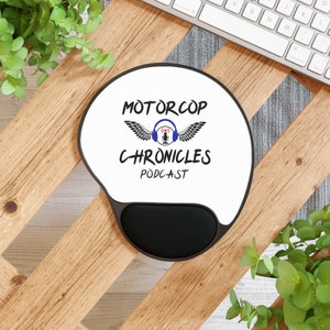 Op de afbeelding: Een ronde witte muismat met een zwart muismatoppervlak. De muismat heeft een zwart-wit logo met de tekst "Motor Cop Chronicles Podcast" met een microfoon en vleugels.