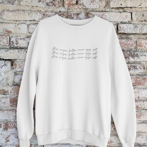 May include: White sweatshirt with the text "flour sugar butter cocoa eggs salt" repeated three times in a handwritten font.