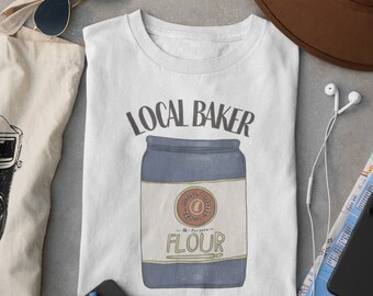 Puede incluir: Camiseta blanca con un gráfico de un tarro de harina azul y blanco con el texto "Local Baker" y "Est. 1988".