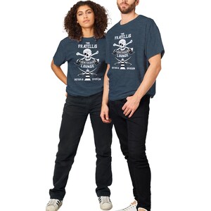 May include: Two people wearing navy blue t-shirts with a white skull and crossbones graphic. The graphic says "The Fratellis Lighthouse Lounge Astoria Oregon".