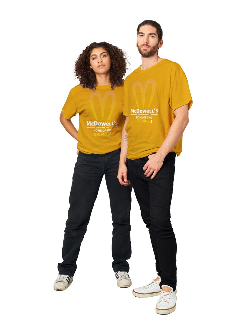 May include: Two people wearing mustard yellow t-shirts with the text "McDowell's HOME OF THE BIG MICK!" and a heart-shaped logo. They are also wearing black jeans and white sneakers. The background is white.