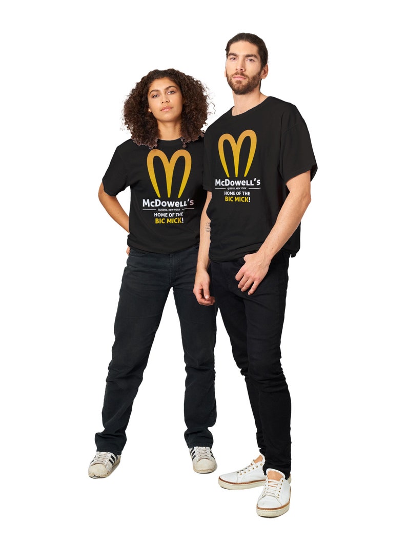 May include: Two people wearing black t-shirts with a gold logo and text that reads "McDowell's HOME OF THE BIG MICK!". The shirts are paired with black jeans and white sneakers. The logo is a stylized golden arch.