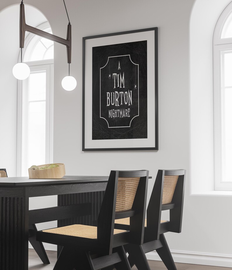 K&ouml;nnte beinhalten: Ein gerahmter Schwarz-Wei&szlig;-Druck mit dem Text "A Tim Burton Nightmare" h&auml;ngt an einer wei&szlig;en Wand. Darunter sind ein schwarzer Esstisch und St&uuml;hle mit gewebten R&uuml;cken zu sehen. &Uuml;ber dem Tisch h&auml;ngt eine moderne Leuchte mit zwei kugelf&ouml;rmigen Gl&uuml;hbirnen.