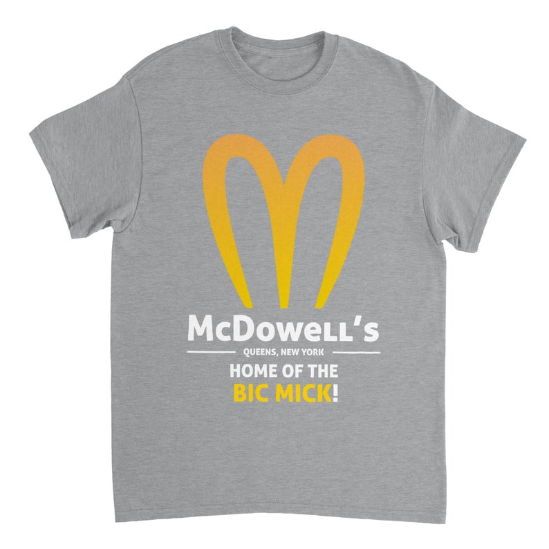 May include: A heather gray t-shirt featuring a stylized yellow and orange heart-shaped logo. Below the logo, the text reads "McDowell's QUEENS, NEW YORK HOME OF THE BIC MICK!" in white.