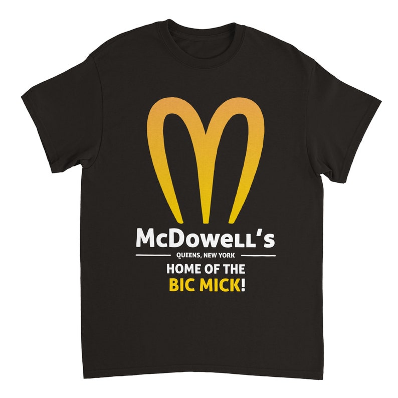 May include: Black t-shirt featuring a yellow and orange heart-shaped logo. The text "McDowell's" is above "QUEENS, NEW YORK" and "HOME OF THE BIC MICK!" in white.