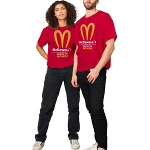 May include: Two people wearing red t-shirts with a gold logo and the text "McDowell's HOME OF THE BIC MICK!". They are also wearing black jeans and white sneakers. The image is set against a white background.
