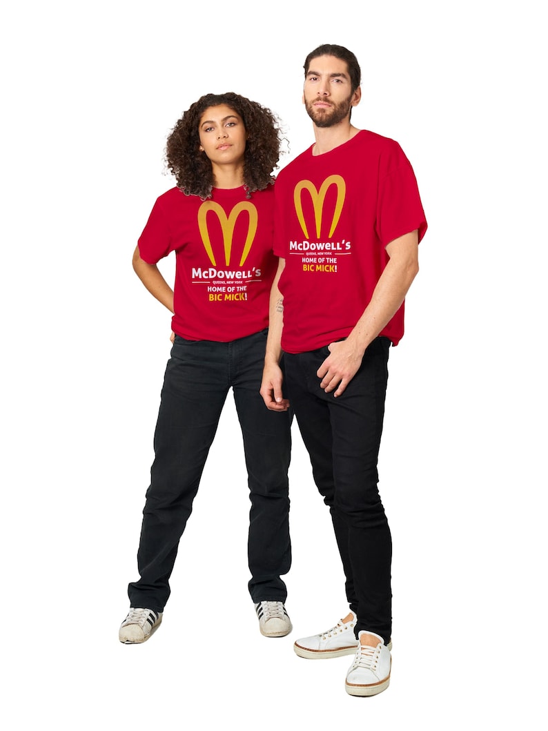 May include: Two people wearing red t-shirts with a gold logo and the text "McDowell's HOME OF THE BIC MICK!". They are also wearing black jeans and white sneakers. The image is set against a white background.