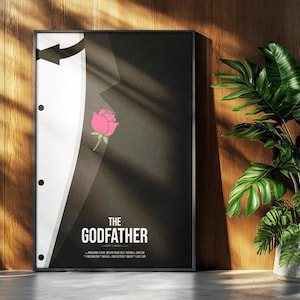May include: Framed poster featuring a minimalist design inspired by "The Godfather" film. The artwork depicts a black suit with a white shirt, a pink rose in the pocket, and the film's title in white text. The poster is displayed against a wooden wall.
