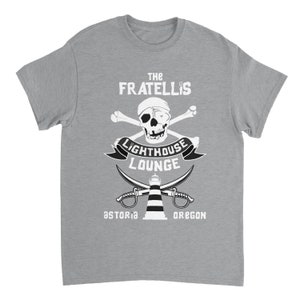 May include: A gray t-shirt with a white graphic design featuring a skull and crossbones, a lighthouse, and the text "The Fratellis Lighthouse Lounge Astoria Oregon".