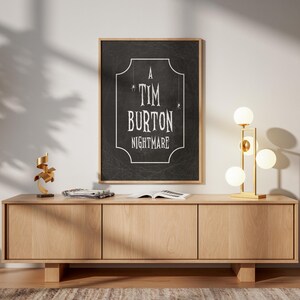 K&ouml;nnte beinhalten: Ein gerahmtes Poster mit dem Text "A Tim Burton Nightmare" in Wei&szlig; auf schwarzem Hintergrund. Das Poster h&auml;ngt &uuml;ber einem hellen Holzschrank. Eine goldene Lampe mit kugelf&ouml;rmigen Gl&uuml;hbirnen und eine kleine Skulptur befinden sich auf dem Schrank.