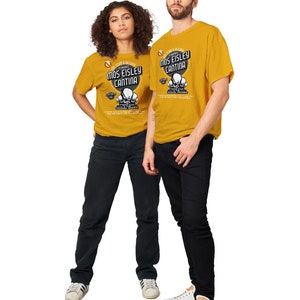 May include: Mustard yellow t-shirts with the text "Mos Eisley Cantina" and a graphic of three skulls. The shirts are worn with black jeans and white sneakers. The image features a man and a woman.