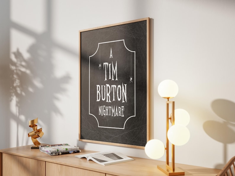 K&ouml;nnte beinhalten: Ein gerahmter Schwarz-Wei&szlig;-Druck mit dem Text "A Tim Burton Nightmare" in einer dekorativen Schriftart. Der Druck befindet sich in einem hellen Holzrahmen und h&auml;ngt an einer wei&szlig;en Wand. Rechts befindet sich eine moderne Lampe mit vier kugelf&ouml;rmigen Lichtern.